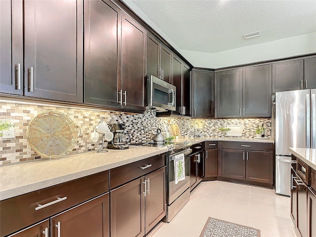 kitchen featuring light tile patterned flooring, appliances with stainless steel finishes, decorative backsplash, dark brown cabinetry, and a textured ceiling