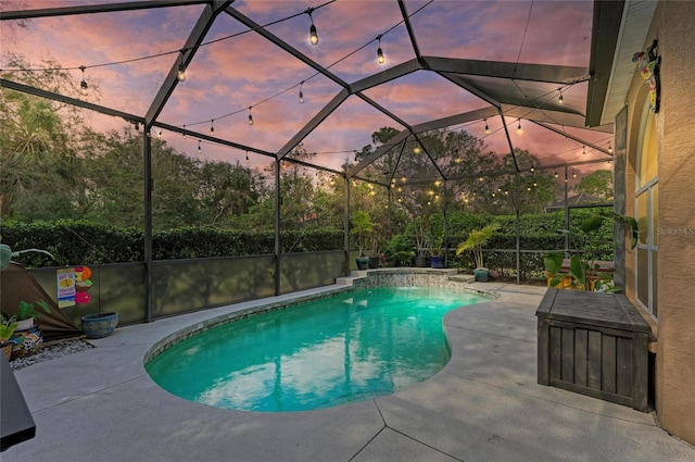 pool at dusk with pool water feature, glass enclosure, and a patio area