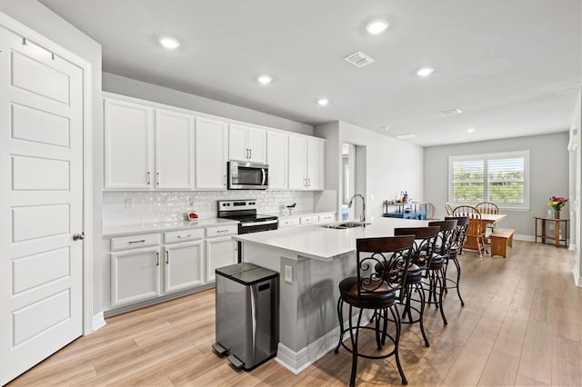44325 Saddlewood Ct, Punta Gorda, FL 33982 - kitchen featuring appliances with stainless steel finishes, light wood-style floors, a kitchen bar, tasteful backsplash, and white cabinetry
