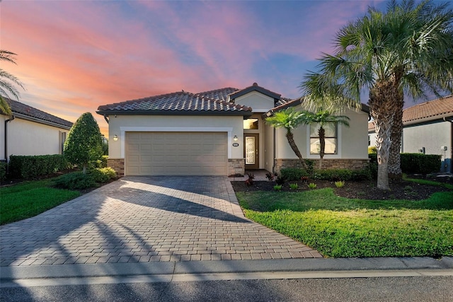 view of front of home featuring decorative driveway, stucco siding, a lawn, an attached garage, and stone siding
