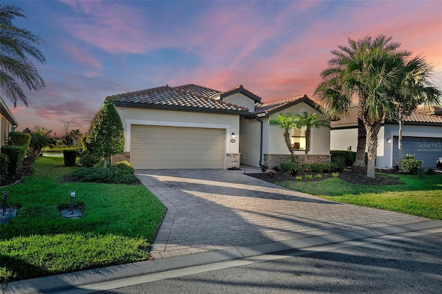 mediterranean / spanish house with a garage, stone siding, stucco siding, decorative driveway, and a front yard