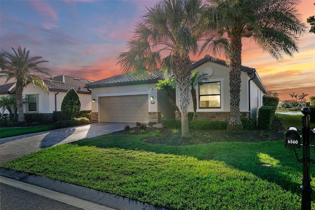 view of front of home with decorative driveway, stucco siding, a front yard, a garage, and stone siding