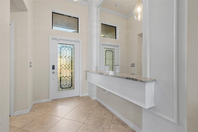 foyer entrance featuring ornamental molding, a towering ceiling, baseboards, and light tile patterned floors