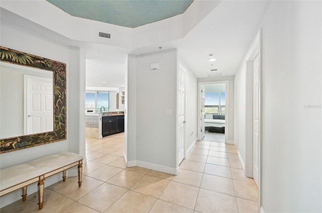 hallway with visible vents, a sink, baseboards, and light tile patterned flooring