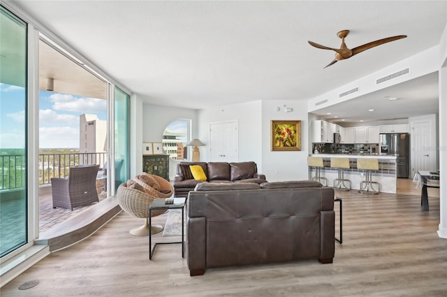 living room with expansive windows, ceiling fan, light wood-style flooring, and visible vents