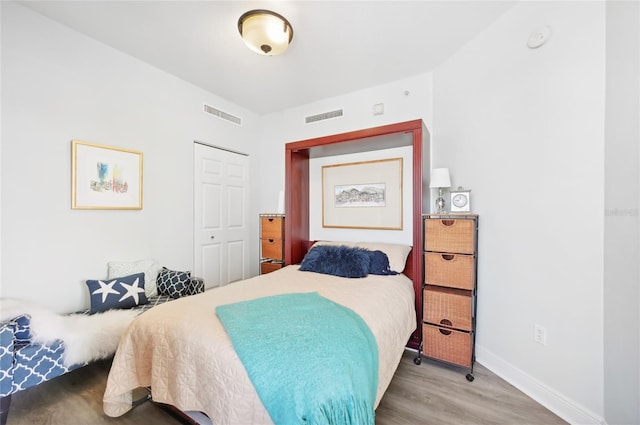 bedroom with baseboards, a closet, visible vents, and wood finished floors