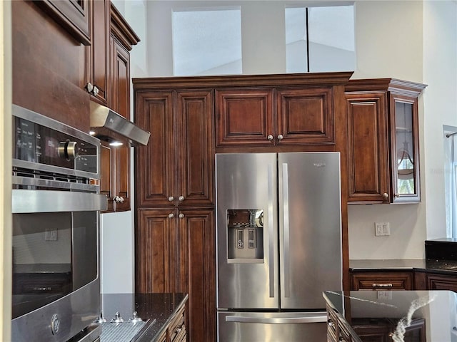 kitchen featuring lofted ceiling, glass insert cabinets, appliances with stainless steel finishes, dark stone countertops, and dark brown cabinets