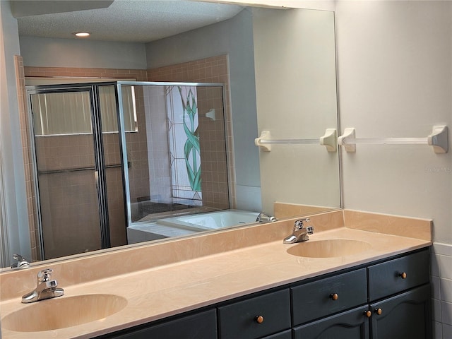 full bath with a sink, a textured ceiling, a shower stall, and double vanity