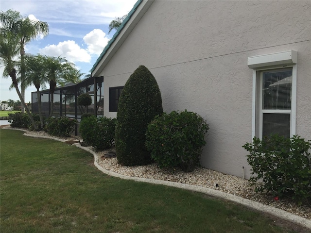 view of side of home with glass enclosure, a lawn, and stucco siding