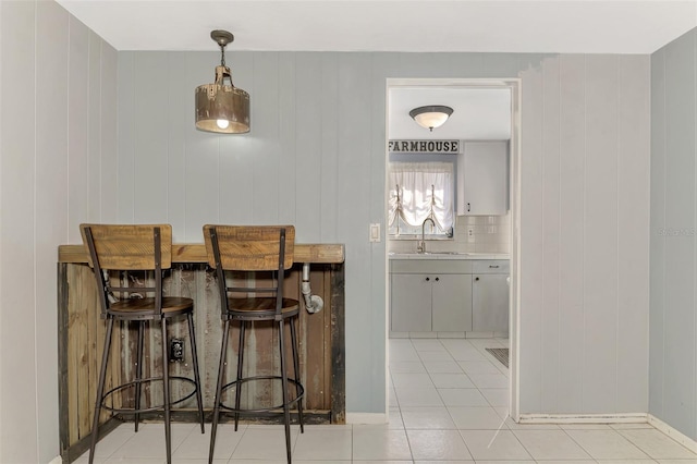 bar with light tile patterned floors, sink, hanging light fixtures, and tasteful backsplash