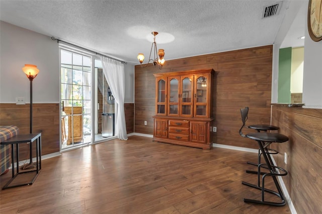 dining space featuring dark wood-type flooring, a textured ceiling, and wood walls