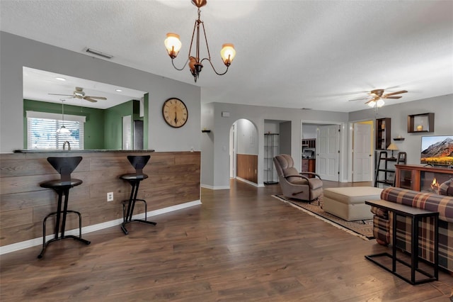 interior space with ceiling fan with notable chandelier, dark wood-type flooring, a textured ceiling, and wood walls