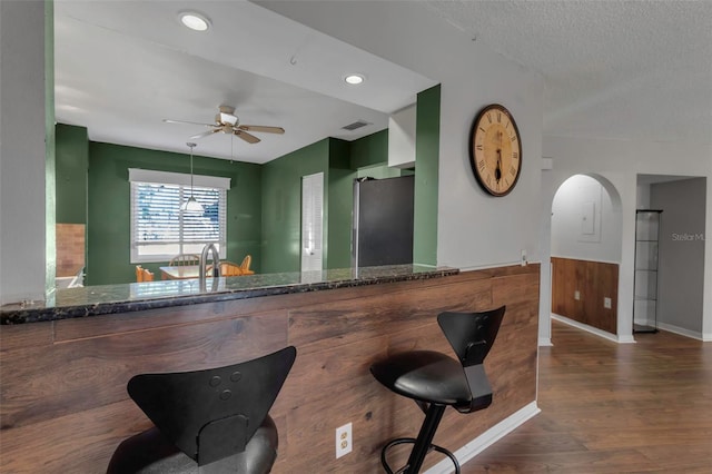 bar with dark hardwood / wood-style floors, dark stone countertops, stainless steel fridge, and a textured ceiling