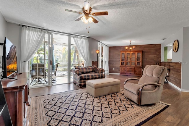 living room featuring hardwood / wood-style flooring, wooden walls, ceiling fan with notable chandelier, and a textured ceiling