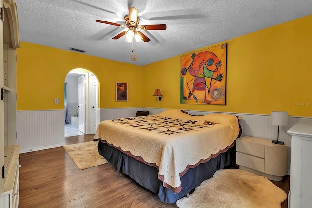 bedroom featuring connected bathroom, hardwood / wood-style floors, a textured ceiling, and ceiling fan