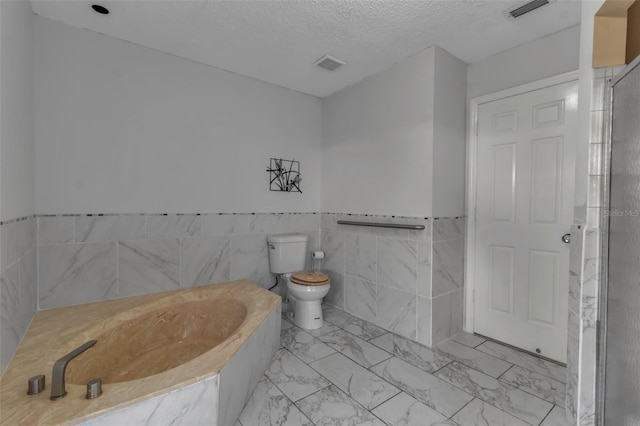 bathroom with toilet, tile walls, a textured ceiling, and a washtub