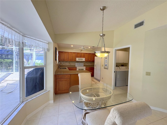 dining space with washer and dryer, a textured ceiling, lofted ceiling, light tile patterned floors, and sink