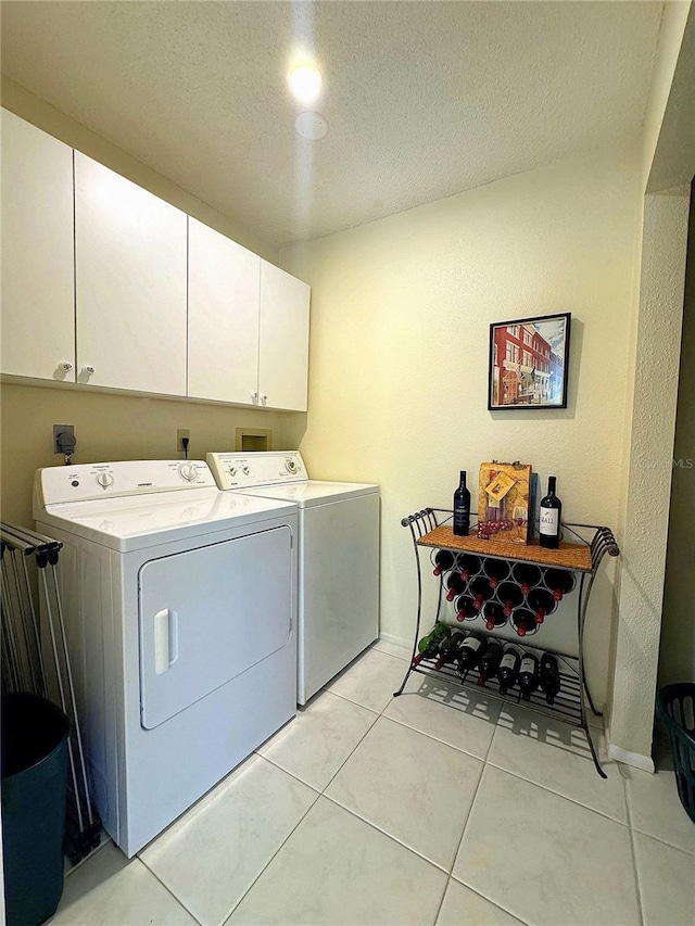 washroom with a textured ceiling, cabinets, independent washer and dryer, and light tile patterned flooring