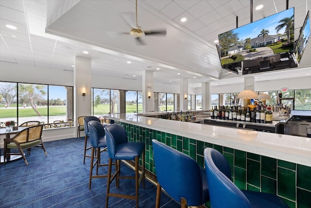 bar featuring ceiling fan, dark carpet, and a wealth of natural light