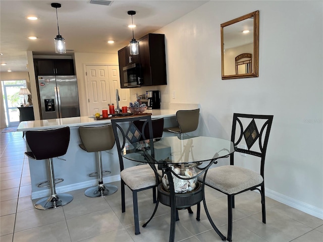 kitchen featuring appliances with stainless steel finishes, pendant lighting, a kitchen bar, light tile patterned floors, and kitchen peninsula