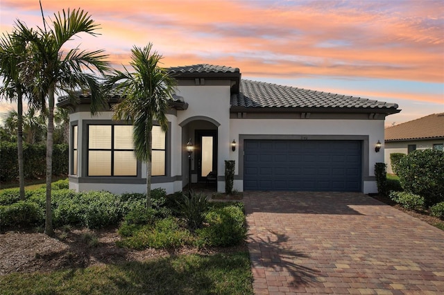 mediterranean / spanish-style house featuring decorative driveway, a tile roof, an attached garage, and stucco siding