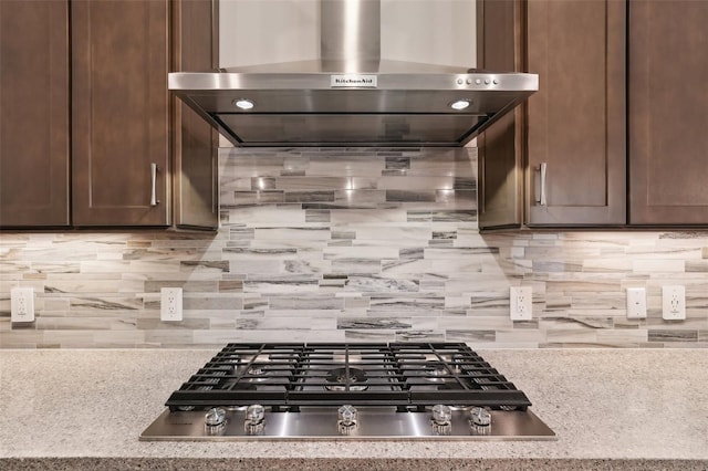 kitchen with stainless steel gas cooktop, wall chimney range hood, light stone counters, and dark brown cabinets