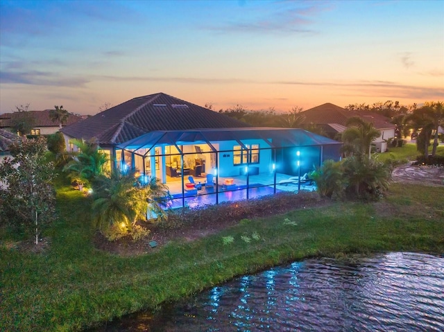 back house at dusk with a water view, a patio, a lanai, and a yard