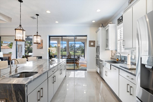 kitchen with a large island, sink, stainless steel appliances, light stone countertops, and white cabinets