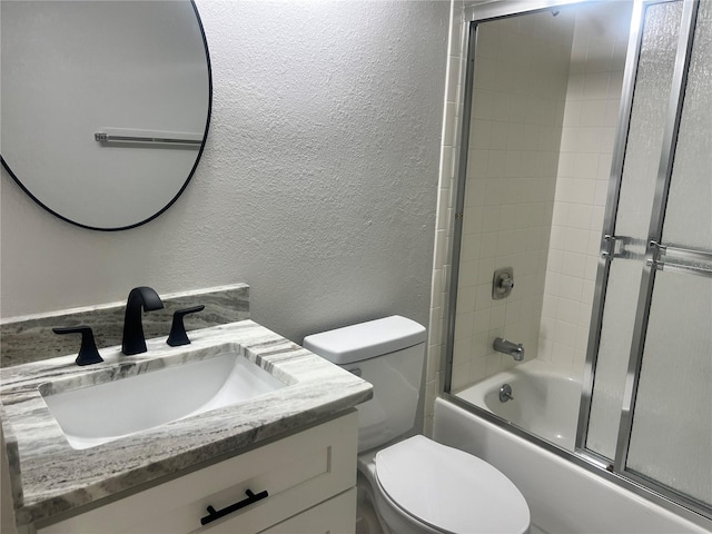 bathroom featuring vanity, toilet, a textured wall, and bath / shower combo with glass door