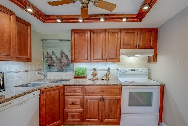 kitchen featuring white appliances, under cabinet range hood, a tray ceiling, and a sink