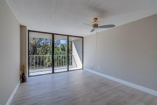 unfurnished room with expansive windows, a textured ceiling, baseboards, and wood finished floors