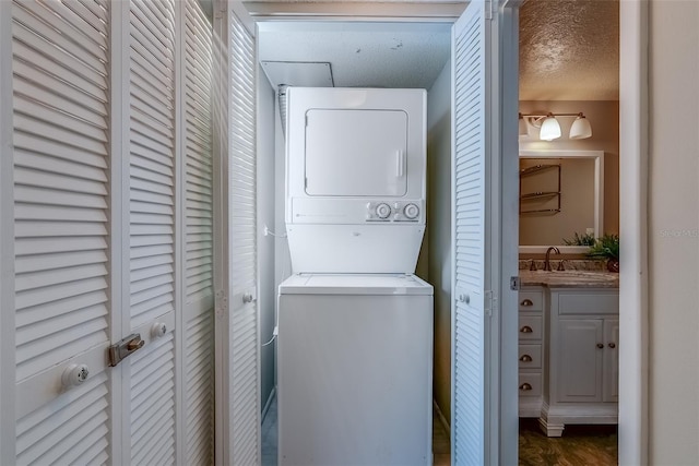 clothes washing area with stacked washer and clothes dryer, a sink, a textured ceiling, and laundry area