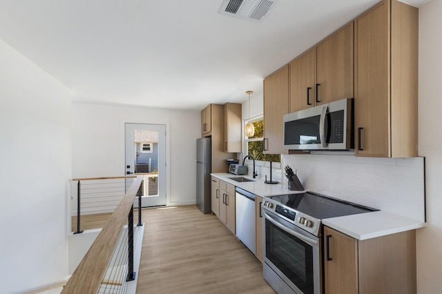 kitchen featuring sink, light wood-type flooring, appliances with stainless steel finishes, pendant lighting, and decorative backsplash