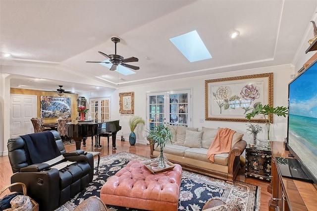 living room featuring ceiling fan, vaulted ceiling with skylight, wood finished floors, ornamental molding, and french doors