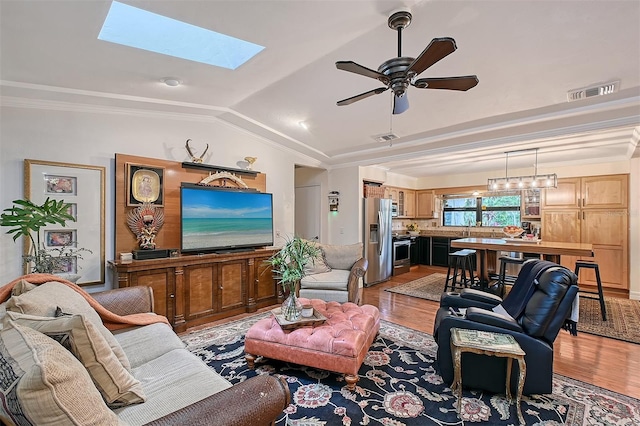 living area featuring visible vents, ornamental molding, lofted ceiling with skylight, and light wood-style flooring