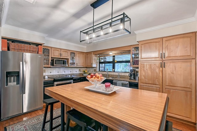 kitchen with ornamental molding, appliances with stainless steel finishes, wood finished floors, and glass insert cabinets