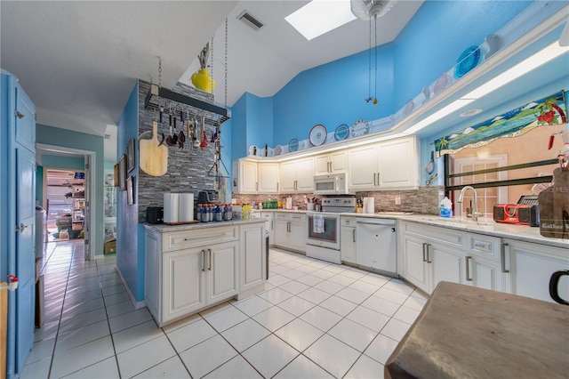 kitchen with a skylight, white cabinetry, sink, light tile patterned floors, and white appliances