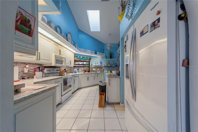 kitchen featuring a skylight, white cabinetry, backsplash, light tile patterned floors, and white appliances