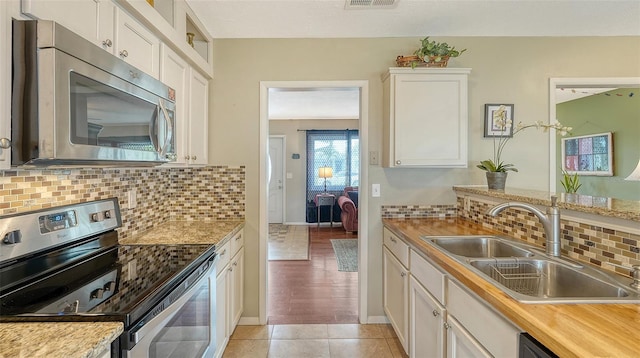 kitchen with light tile patterned floors, white cabinets, decorative backsplash, appliances with stainless steel finishes, and a sink