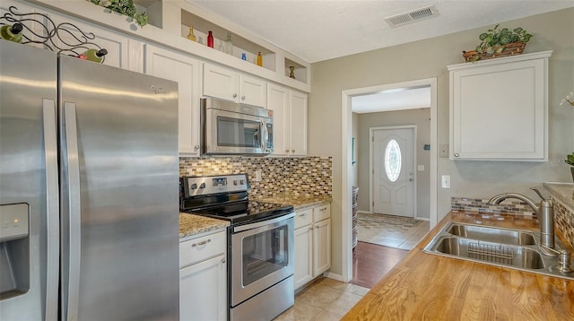 kitchen featuring light tile patterned floors, stainless steel appliances, tasteful backsplash, visible vents, and a sink