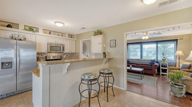 kitchen featuring visible vents, decorative backsplash, appliances with stainless steel finishes, white cabinets, and a kitchen bar