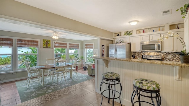 kitchen featuring visible vents, a peninsula, light stone countertops, stainless steel appliances, and backsplash