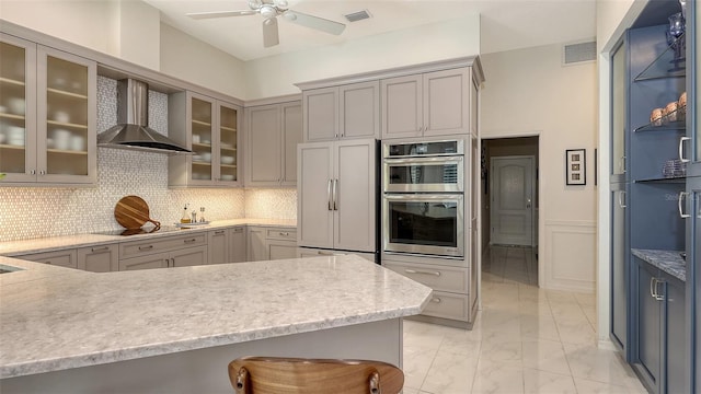 kitchen with wall chimney exhaust hood, glass insert cabinets, light countertops, double oven, and paneled fridge