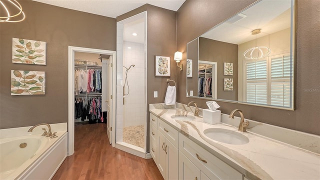 bathroom featuring wood finished floors, a garden tub, a walk in closet, vanity, and a shower stall