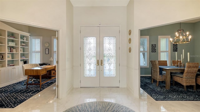 foyer featuring french doors, a healthy amount of sunlight, a high ceiling, and an inviting chandelier