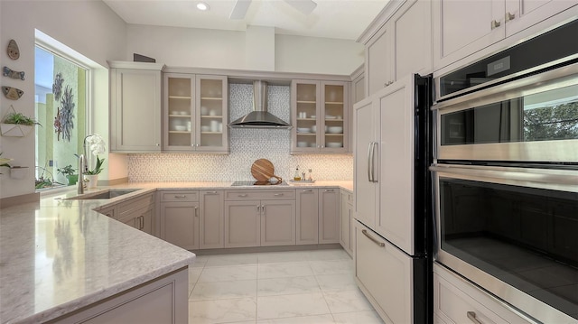 kitchen with paneled built in fridge, a sink, marble finish floor, wall chimney range hood, and glass insert cabinets