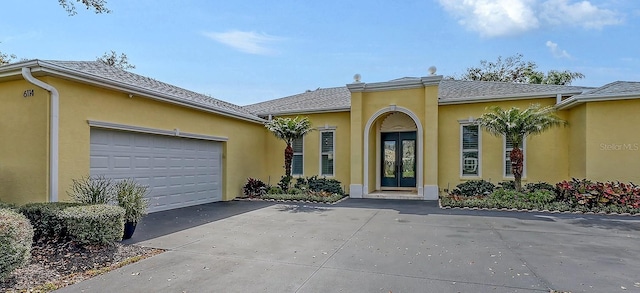 property entrance with a garage, french doors, driveway, and stucco siding