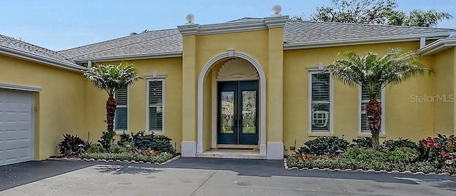 doorway to property featuring french doors, roof with shingles, an attached garage, and stucco siding