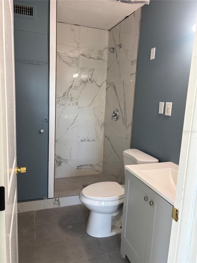 bathroom featuring vanity, a tile shower, and toilet