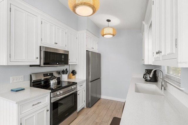 kitchen featuring white cabinets, stainless steel appliances, light countertops, pendant lighting, and a sink